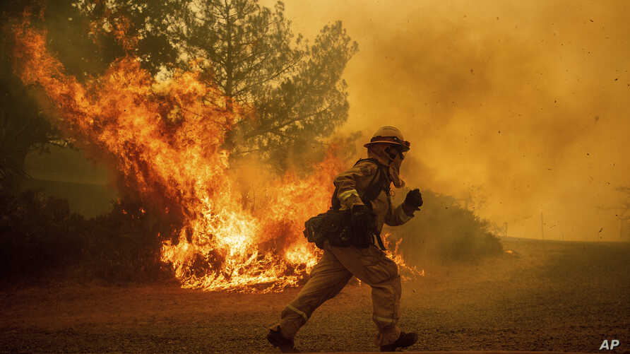 A firefighter runs while trying to save a home as a wildfire tears through Lakeport, Calif., Tuesday, July 31, 2018. (AP Photo/Noah Berger, File)